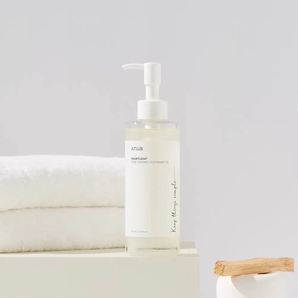 Anua cleansing oil for sensitive skin in clear pump bottle next to white towels on cream surface